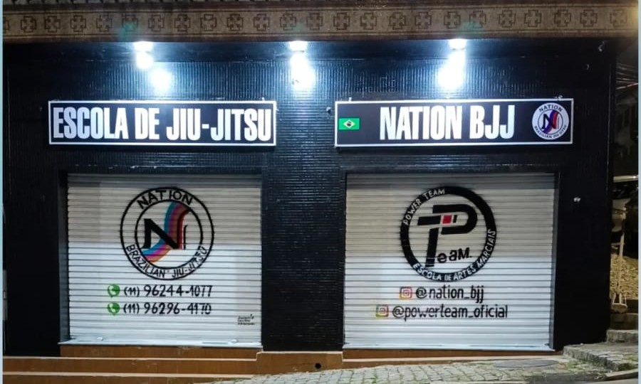 Fachada da Nation BJJ à noite, com a placa Escola de Jiu-Jitsu e as logos da Nation e da Power Team