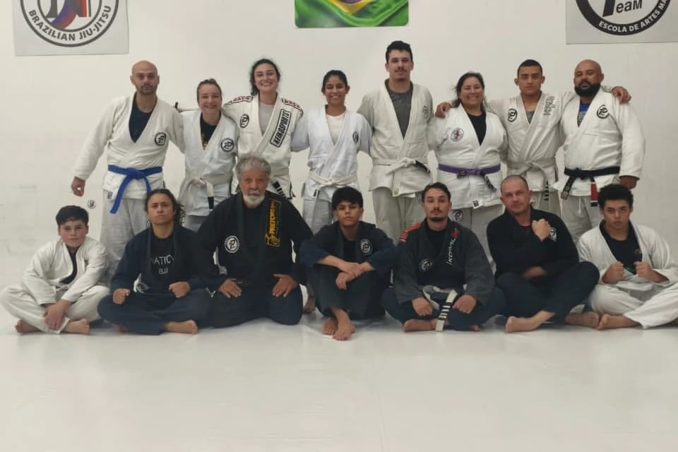 Professores e alunos da Nation BJJ, de kimono, com faixas azul, roxa e preta, no tatame
