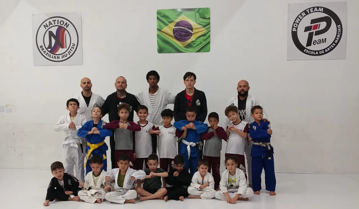 Turma Kids da Nation BJJ, crianças pequenas de kimono fazendo pose com os professores atrás
