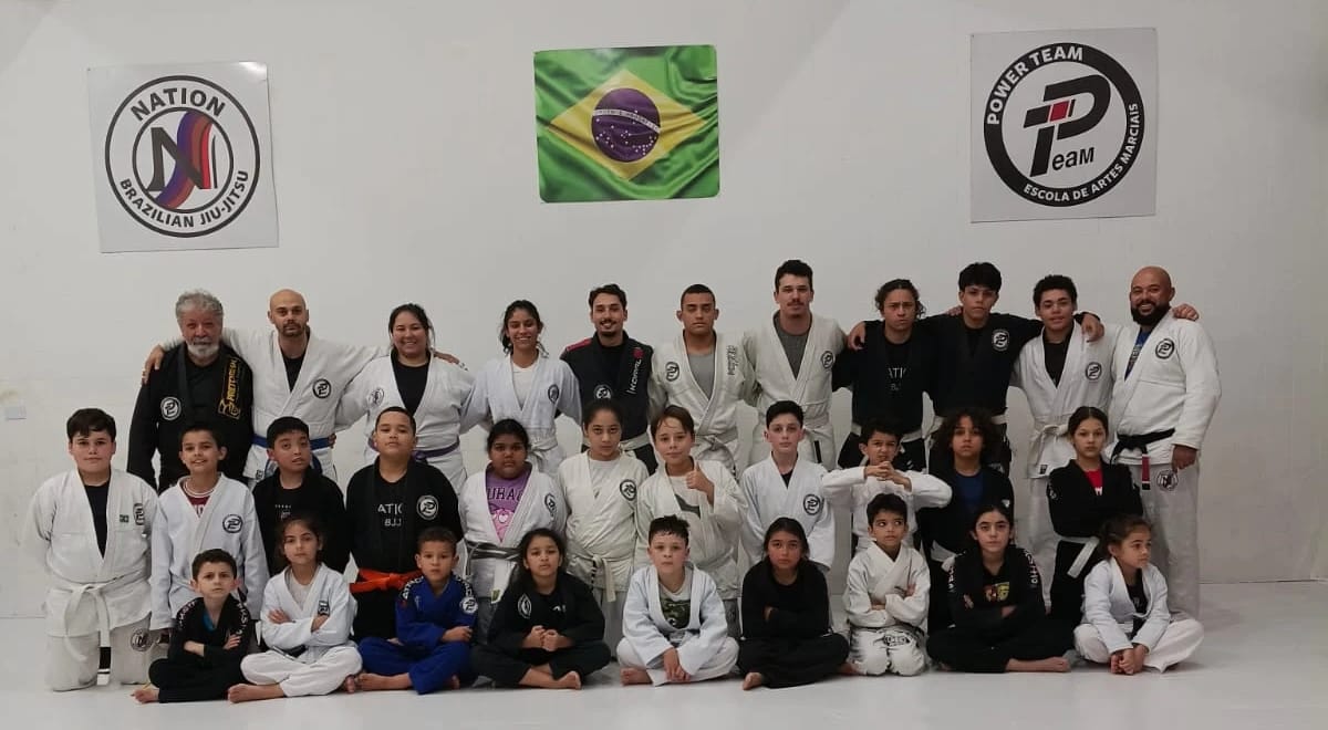 Crianças, jovens e adultos de kimono posando juntos no tatame da Nation BJJ